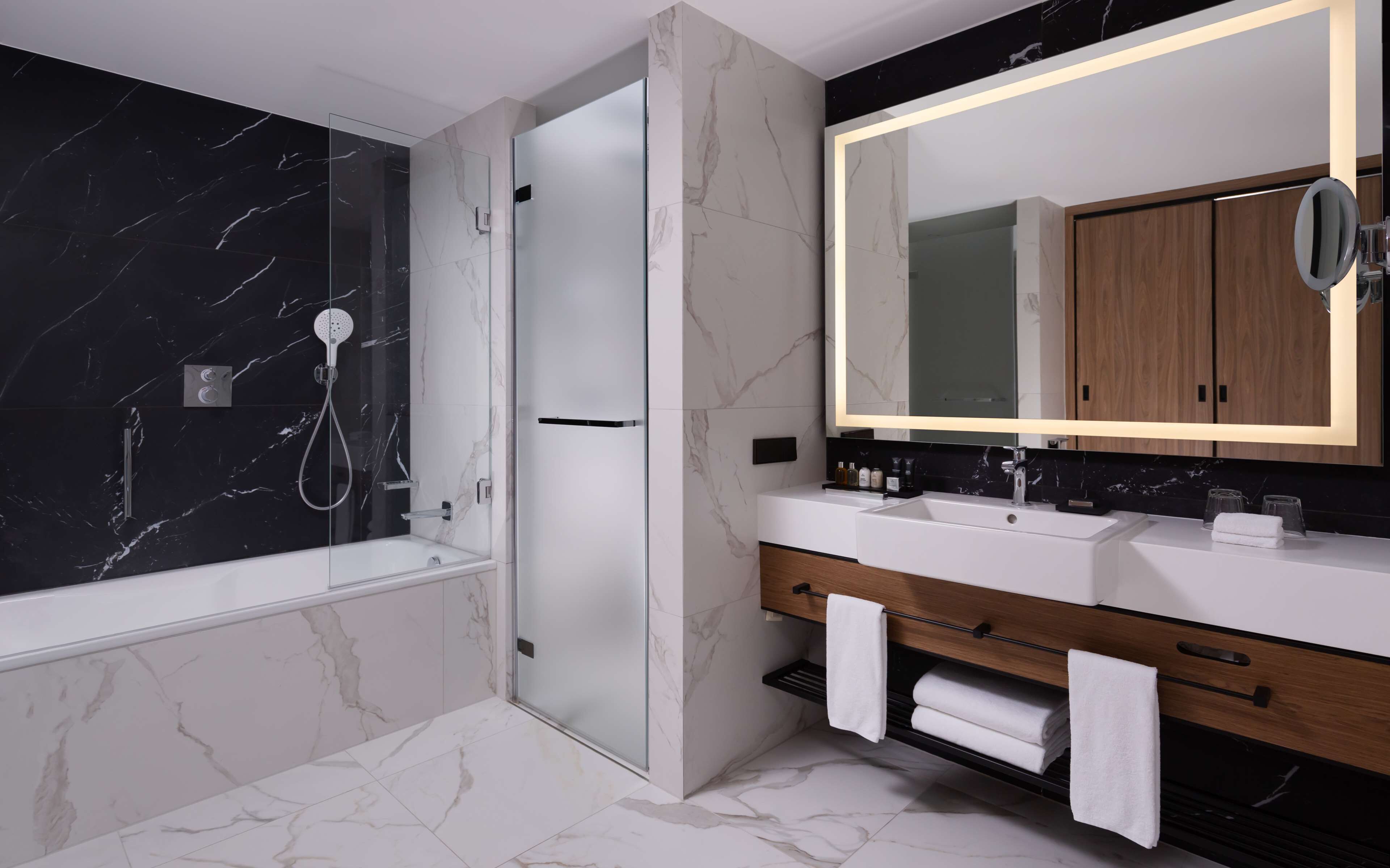 A modern bathroom with a glass-enclosed shower, a large mirror, and a vanity with a wooden cabinet.