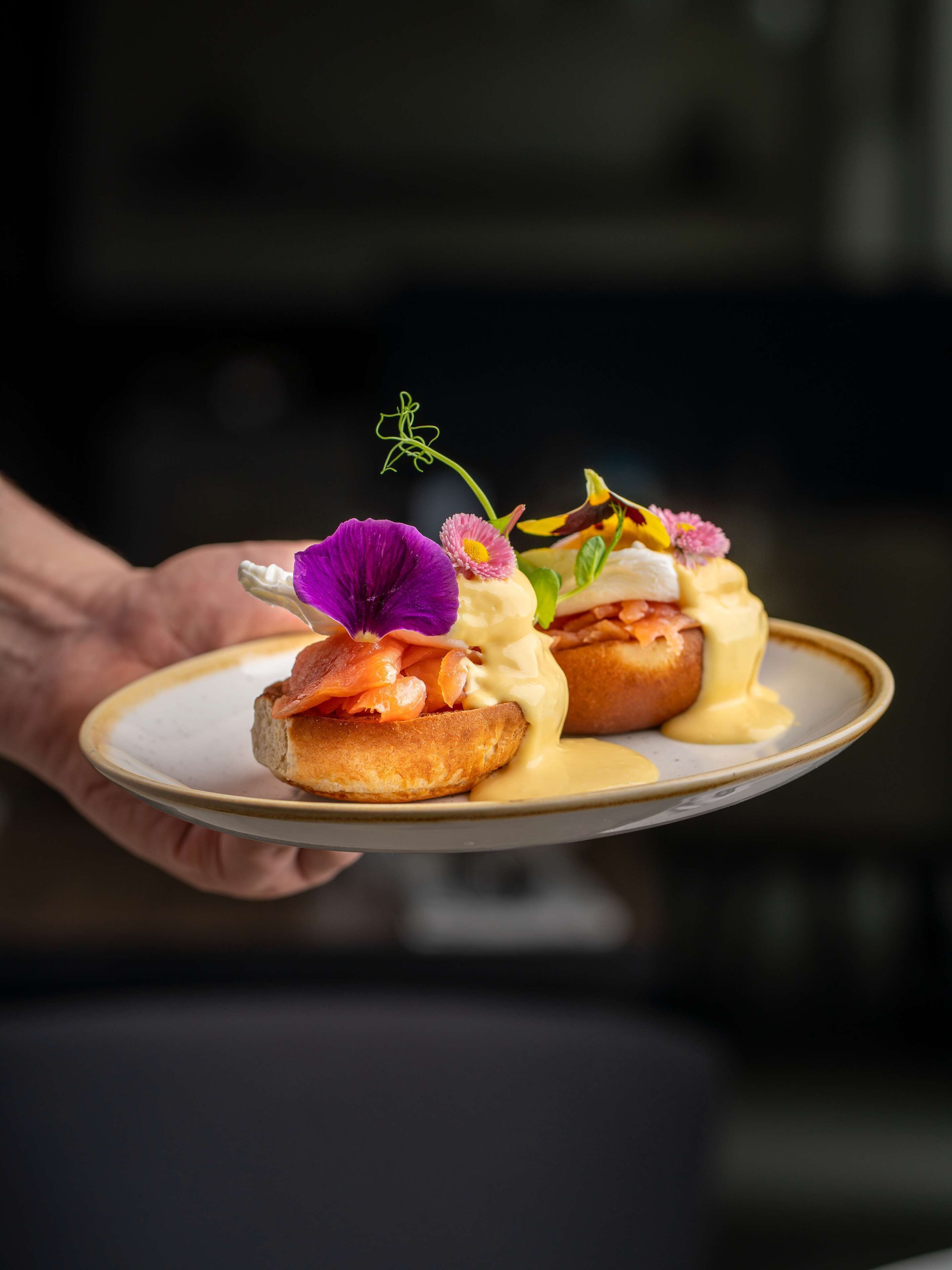 Un plato con varios alimentos, incluyendo un pastel de salmón y salsa, sostenido por una persona.