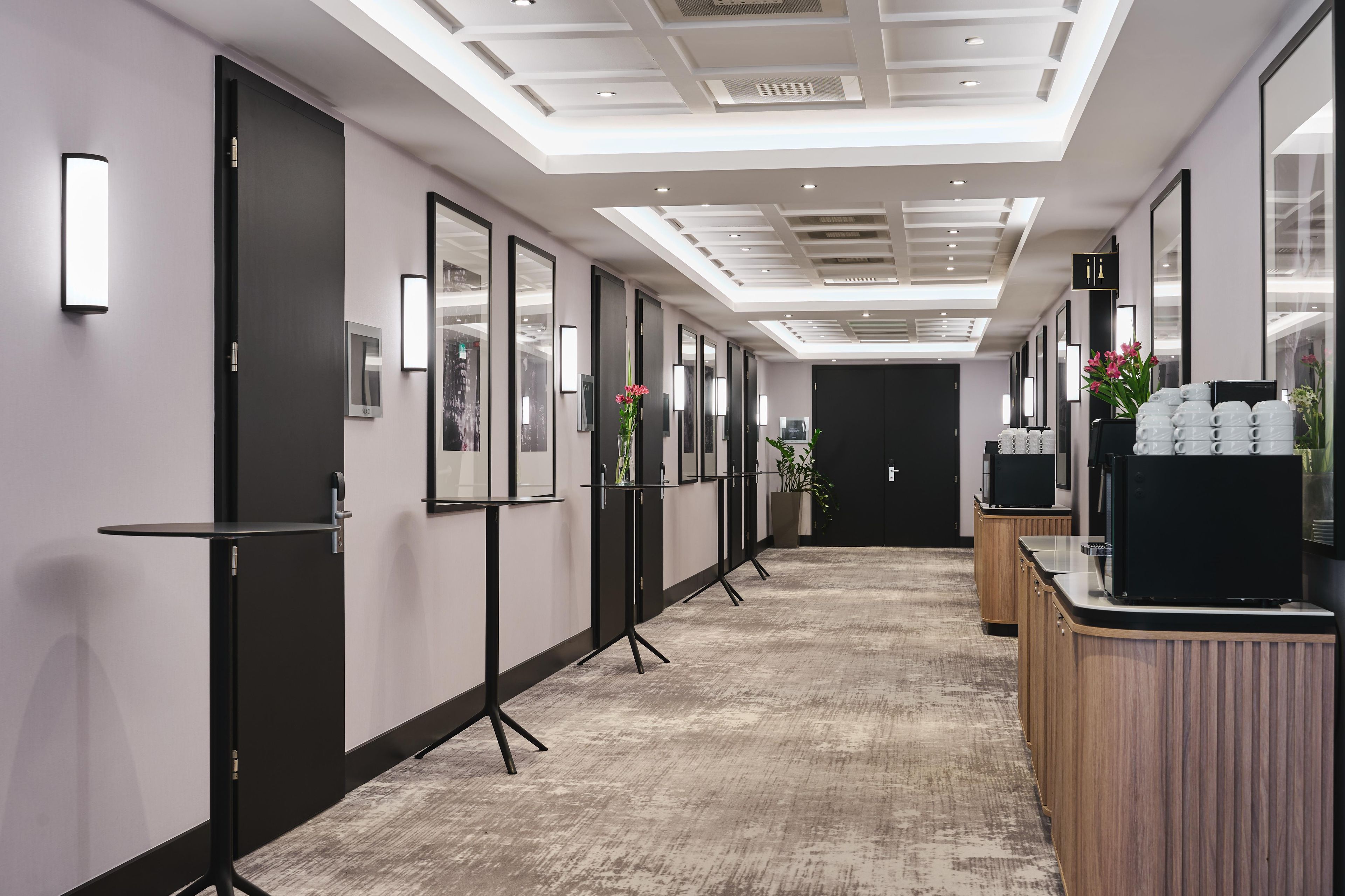 A hallway with framed pictures on the walls, a reception desk with a coffee machine, and a modern ceiling design.