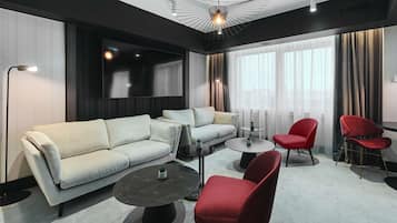 A modern living room with a sofa, red chairs, a coffee table, and a TV mounted on the wall.