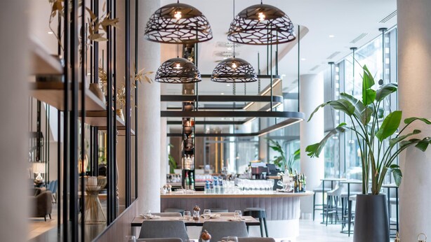 A modern restaurant with a long dining table, multiple chairs, hanging pendant lights, and a large potted plant. - Radisson Collection Hotel, Warsaw (Warsaw)