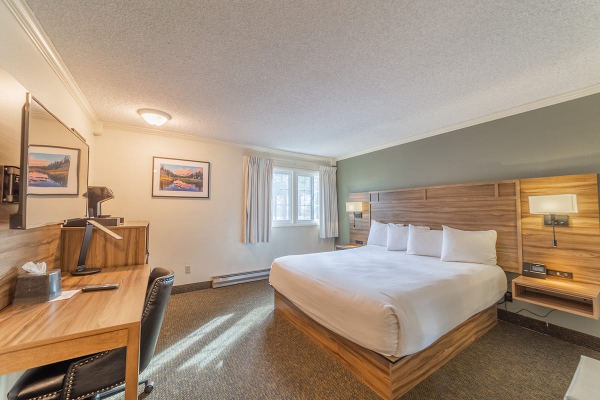 A hotel room with a large bed, a desk with a chair, a desk lamp, a nightstand with a lamp, and two framed pictures on the wall.