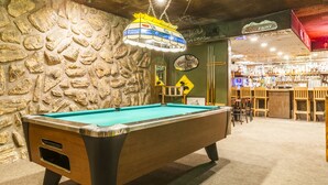 Una mesa de billar en una zona de bar con un fondo de pared de piedra y una barra llena de botellas.