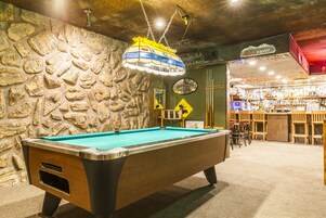 A pool table in a bar area with a stone wall backdrop and a bar stocked with bottles.