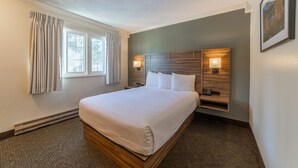 Una habitación de hotel con una cama grande, lámparas de noche, una mesita de noche y un ventanal con cortinas.