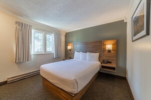 A hotel room with a large bed, bedside lamps, a nightstand, and a window with curtains.