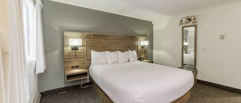 A hotel room with a large bed, wooden headboard, two bedside tables with lamps, a mirror, and a carpeted floor.