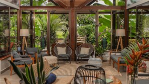 A spacious indoor area with large windows, wicker furniture, and potted plants.