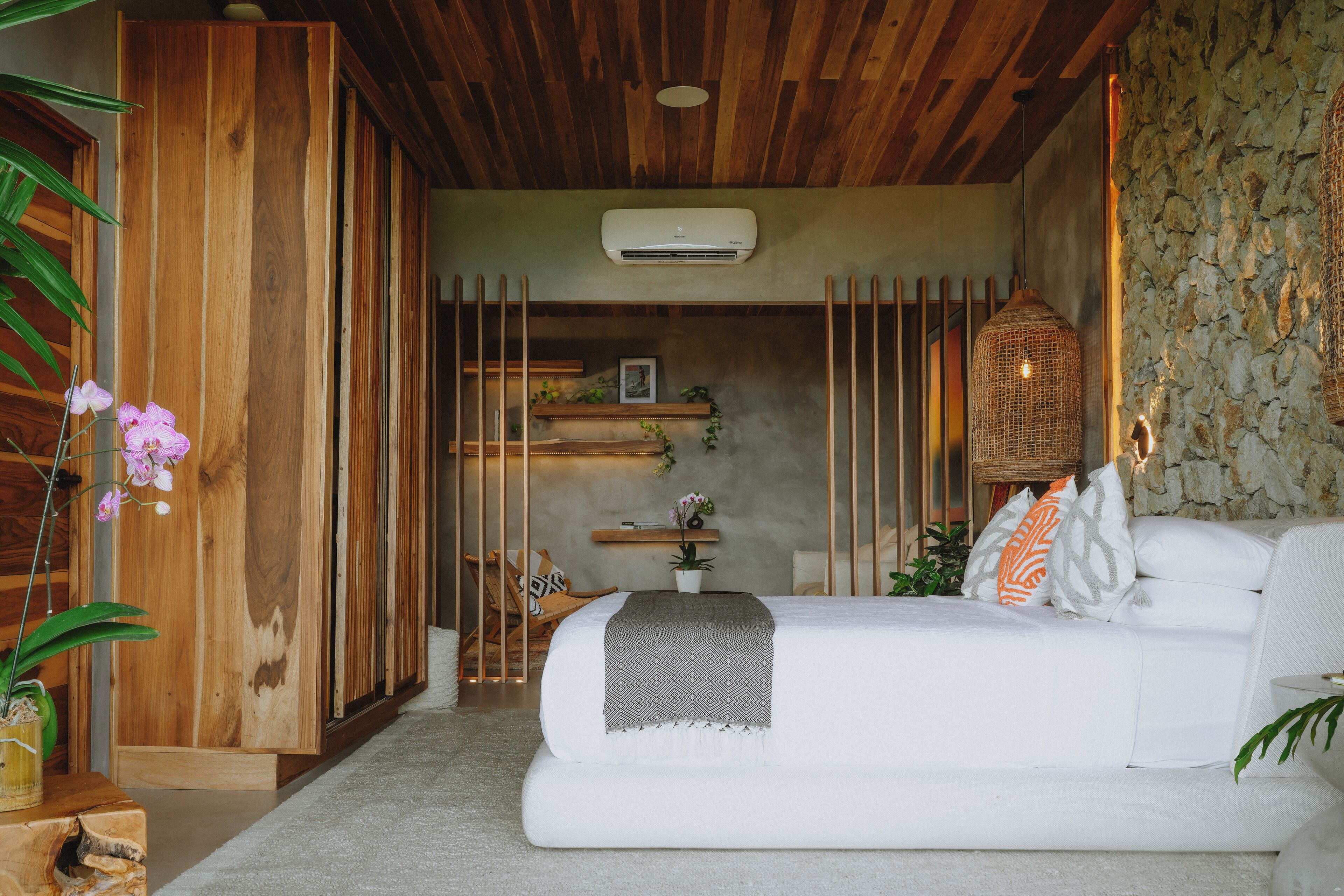 A modern bedroom with a white sofa, a wooden wardrobe, a stone wall, and a hanging light fixture.