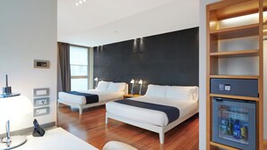 A hotel room with two beds, a desk with a lamp, a mini-fridge, and a large window. - Hotel Plaza Venice (Mestre)