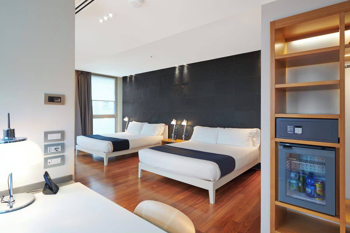 Une chambre d’hôtel avec deux lits, un bureau avec une lampe, un mini-réfrigérateur et une grande fenêtre.