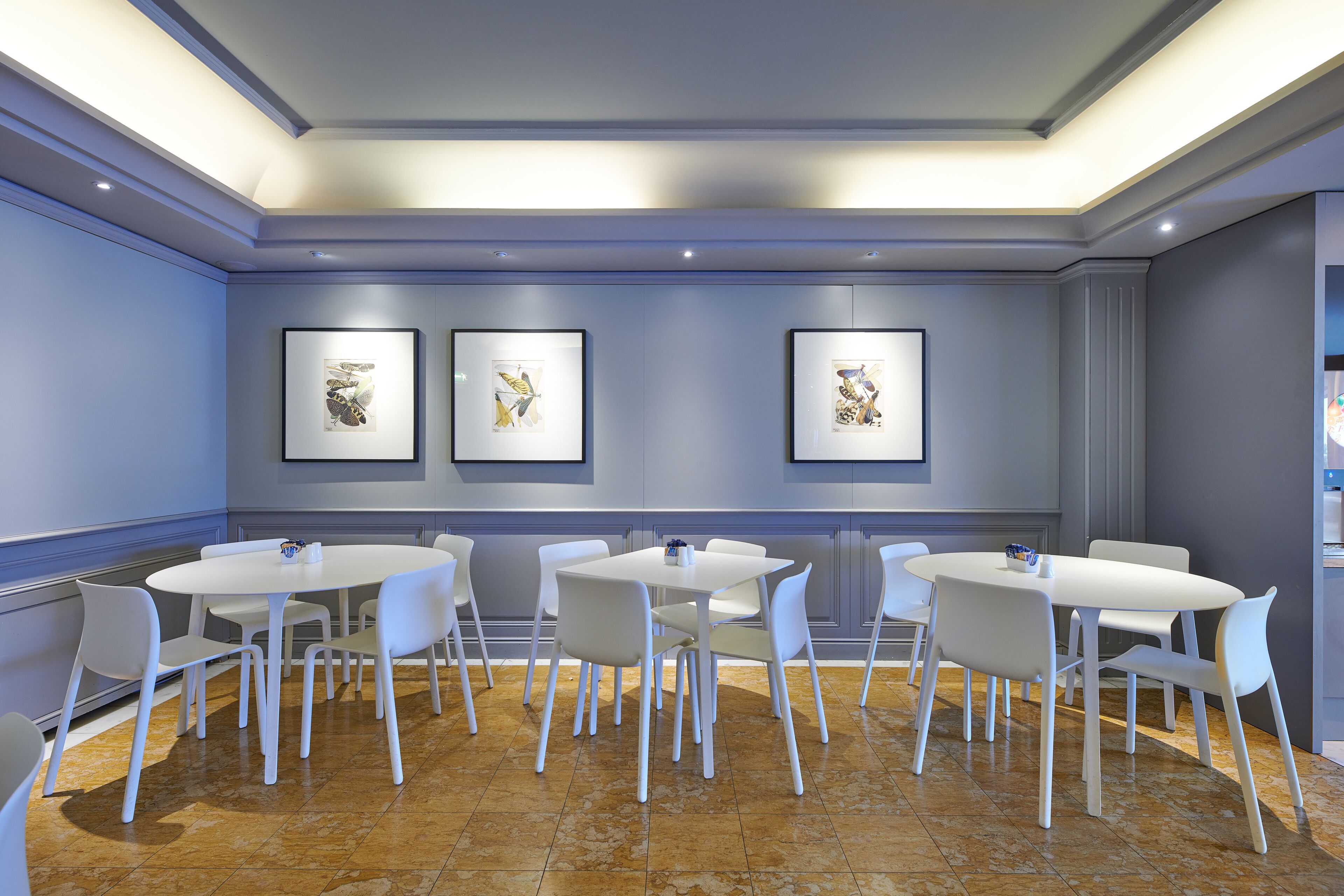 A modern conference room with white tables and chairs, framed artwork on the walls, and a polished tile floor.