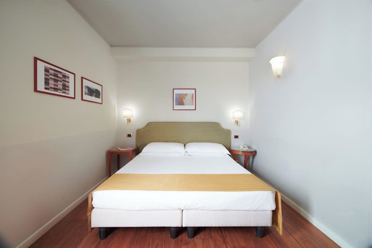 Une chambre d’hôtel bien aménagée, avec un grand lit, deux tables de chevet et des œuvres d’art encadrées accrochées aux murs.