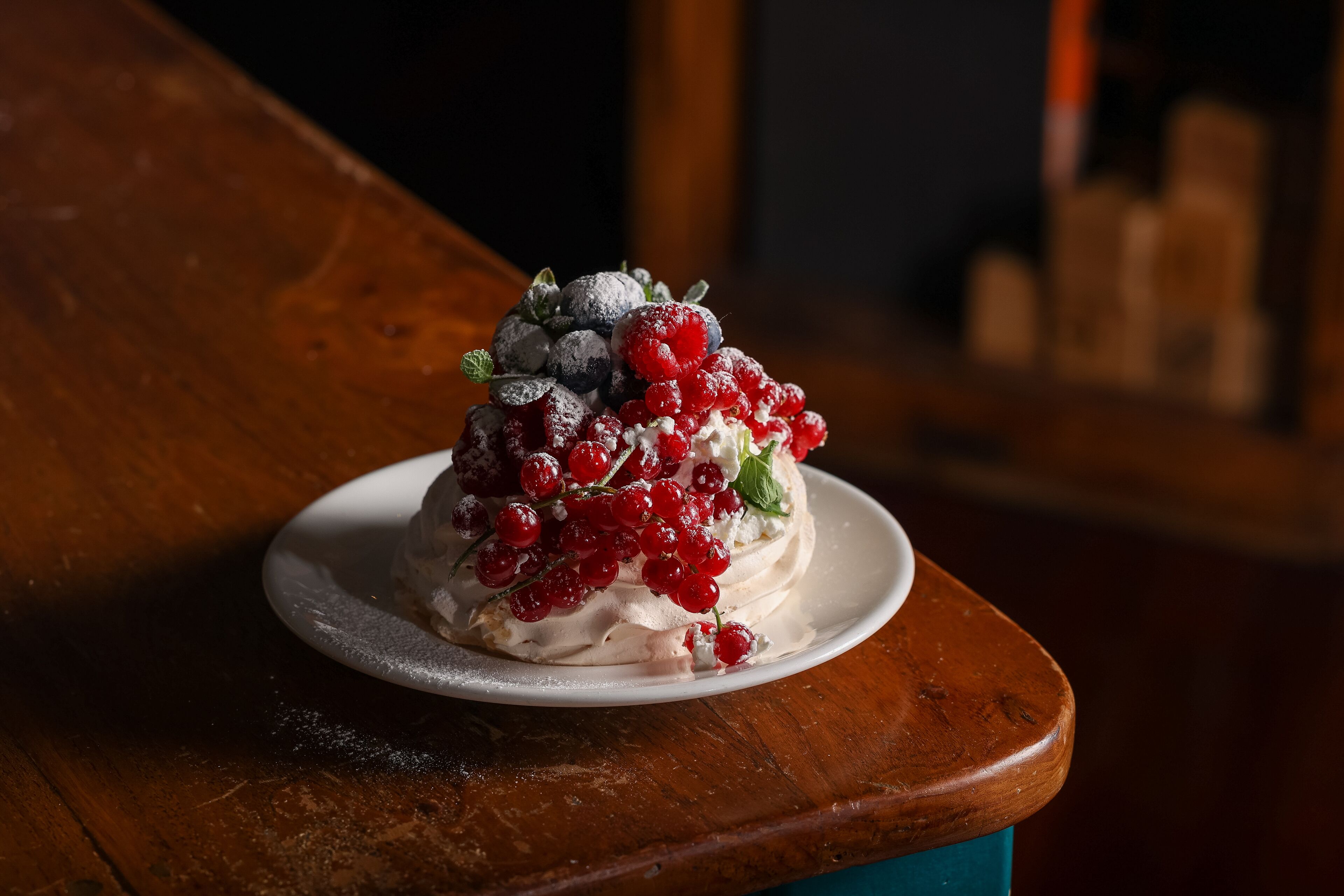 A dessert on a white plate with berries and powdered sugar on a wooden table.