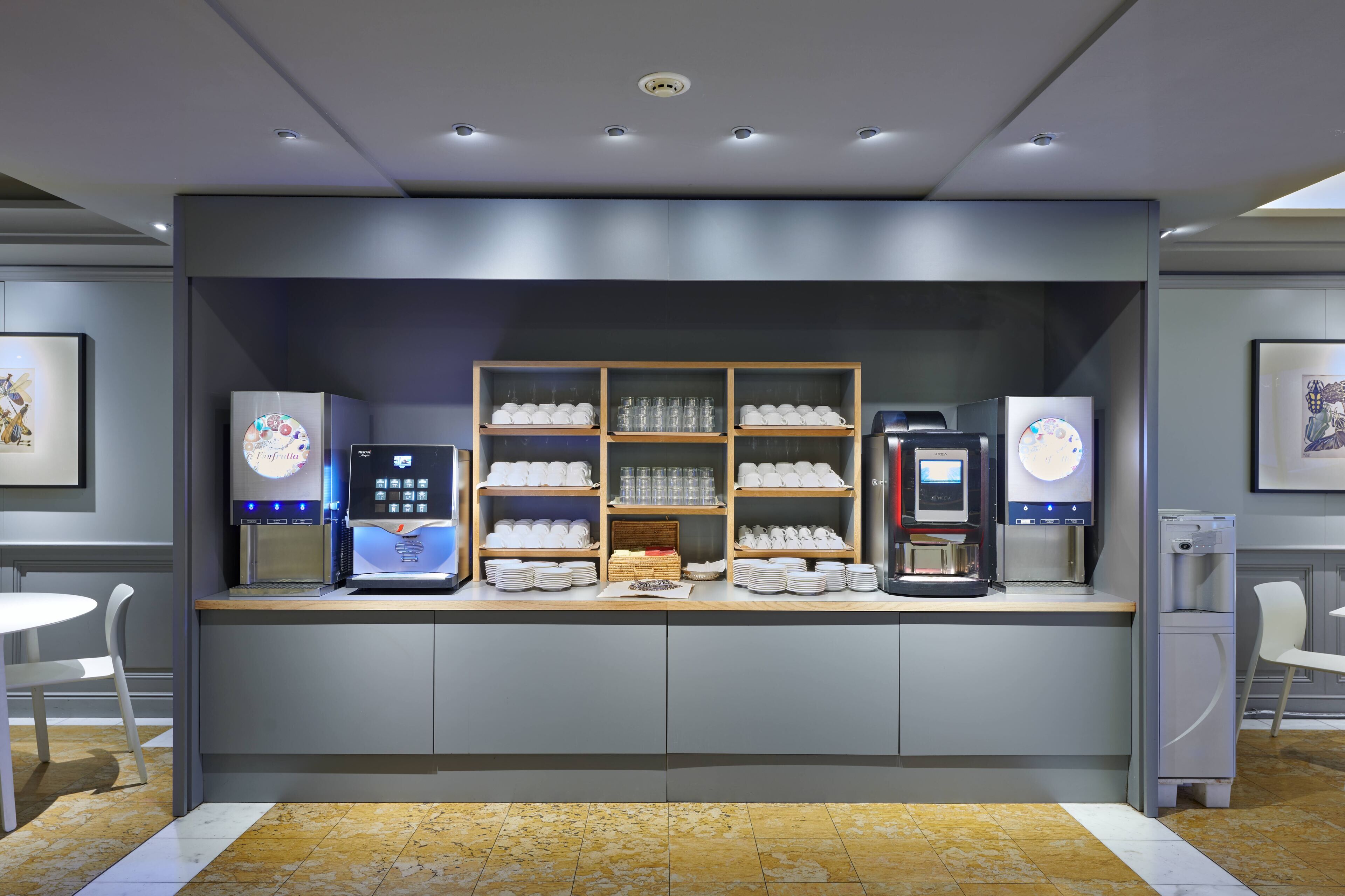 A self-service beverage station with multiple coffee machines and a glass display case.