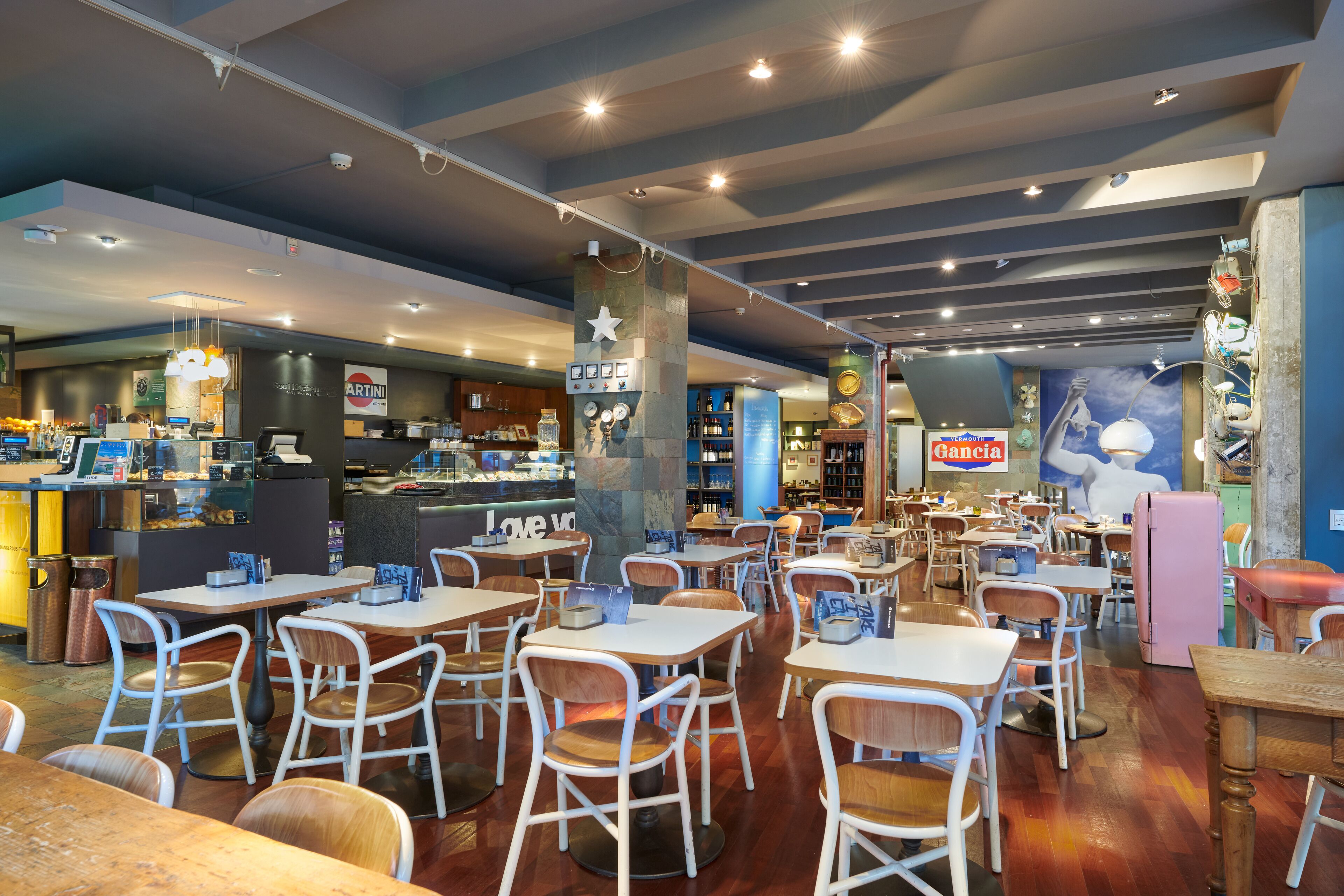 A restaurant with multiple tables and chairs, a bar area, and a counter with a menu.