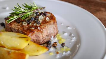 A plate with a grilled steak, roasted potatoes, and a garnish of rosemary and black peppercorns.