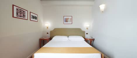 Una habitación de hotel ordenada con una cama grande, dos mesitas de noche y lámparas de pared.