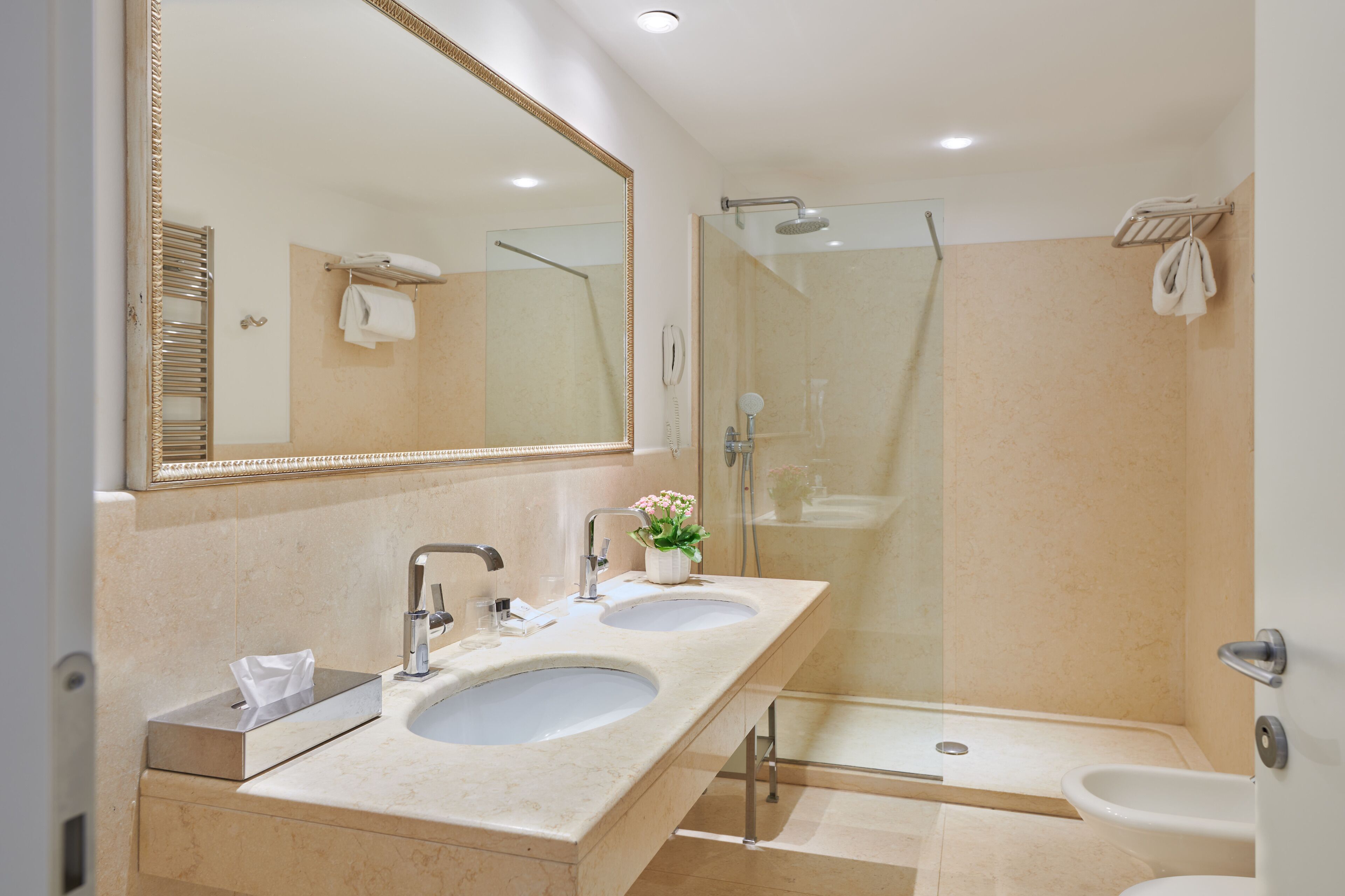 A modern bathroom with two sinks, a large mirror, a glass-enclosed shower, and a toilet.