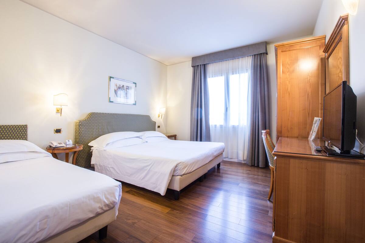 Une chambre d’hôtel avec deux lits, une commode en bois, un téléviseur et un tableau encadré au mur.