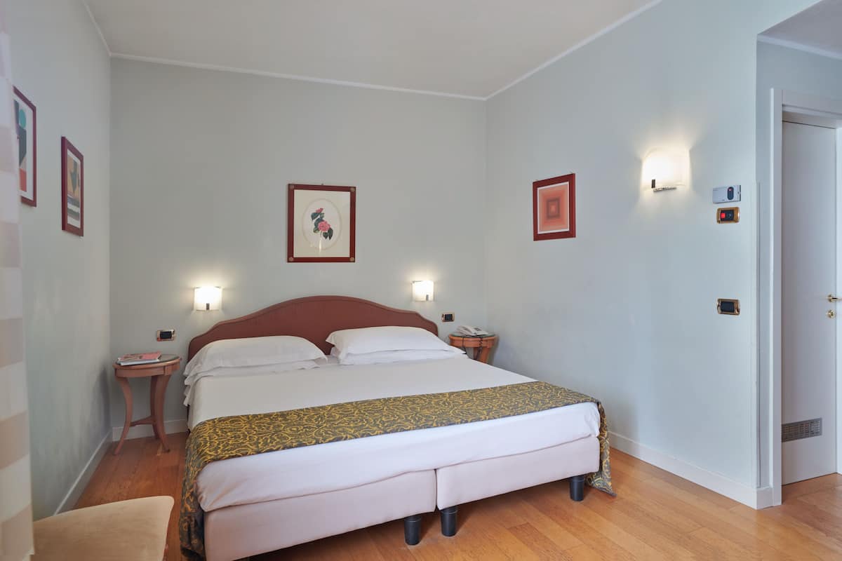 Une chambre à coucher bien rangée, avec un grand lit, des tables de chevet et des tableaux encadrés accrochés aux murs.