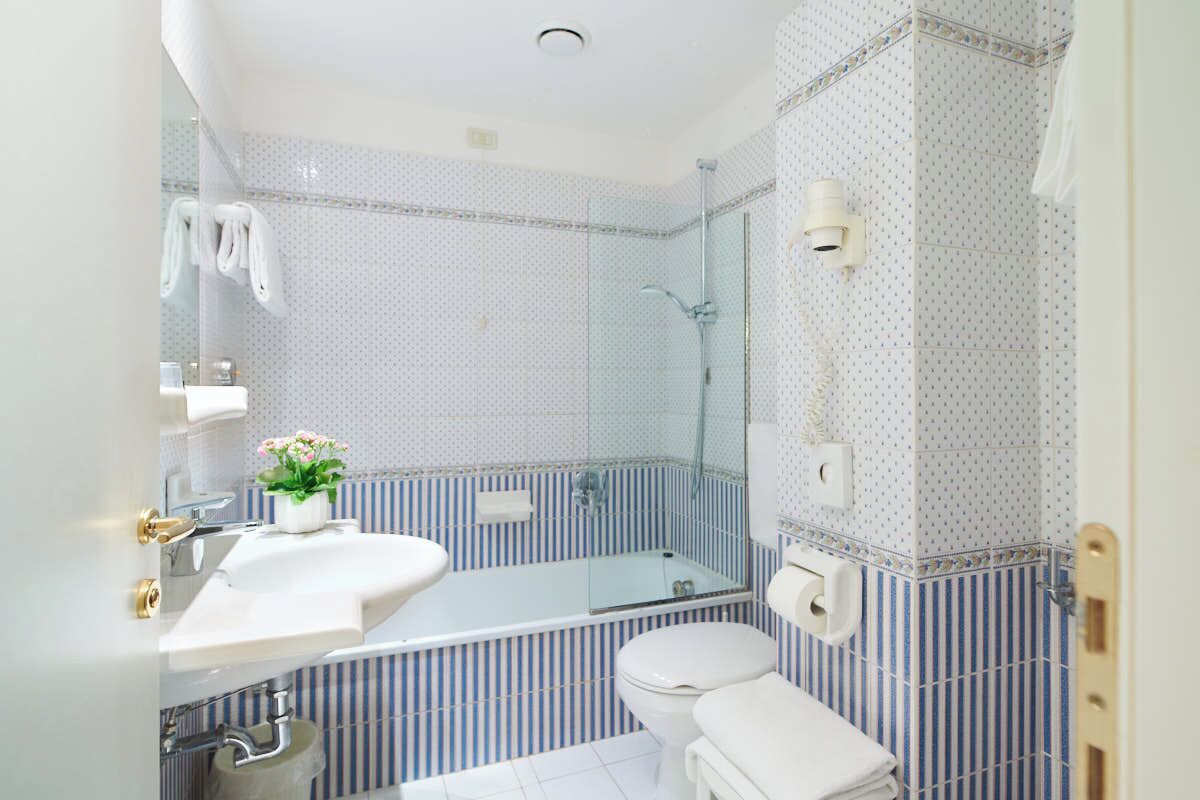 Un baño con lavamanos blanco, cabina de ducha de vidrio, inodoro y perchero para toallas.