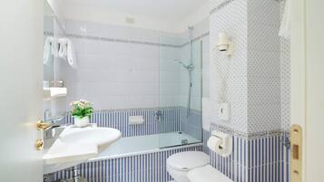 Un baño con lavamanos blanco, cabina de ducha de vidrio, inodoro y perchero para toallas.