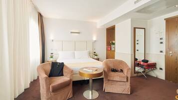 A hotel room with a bed, two armchairs, a small round table, a suitcase, and a mirror.