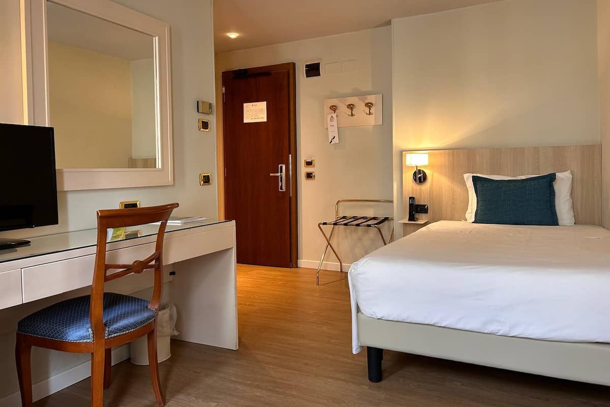 Une chambre d’hôtel avec un lit, un bureau et une chaise, une télévision et une porte.