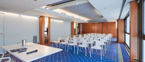 A conference room with a white table, multiple white chairs, and a blue patterned carpet.