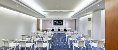 A conference room with a blue carpet, white chairs, a table, and a sign reading "PLAZA VENICE MESTRE".