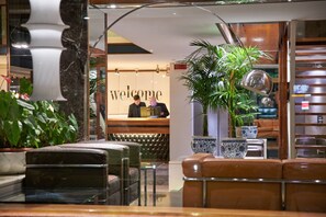 A reception area with a 'Welcome' sign, a receptionist, a potted plant, and a seating area with a sofa and a table.