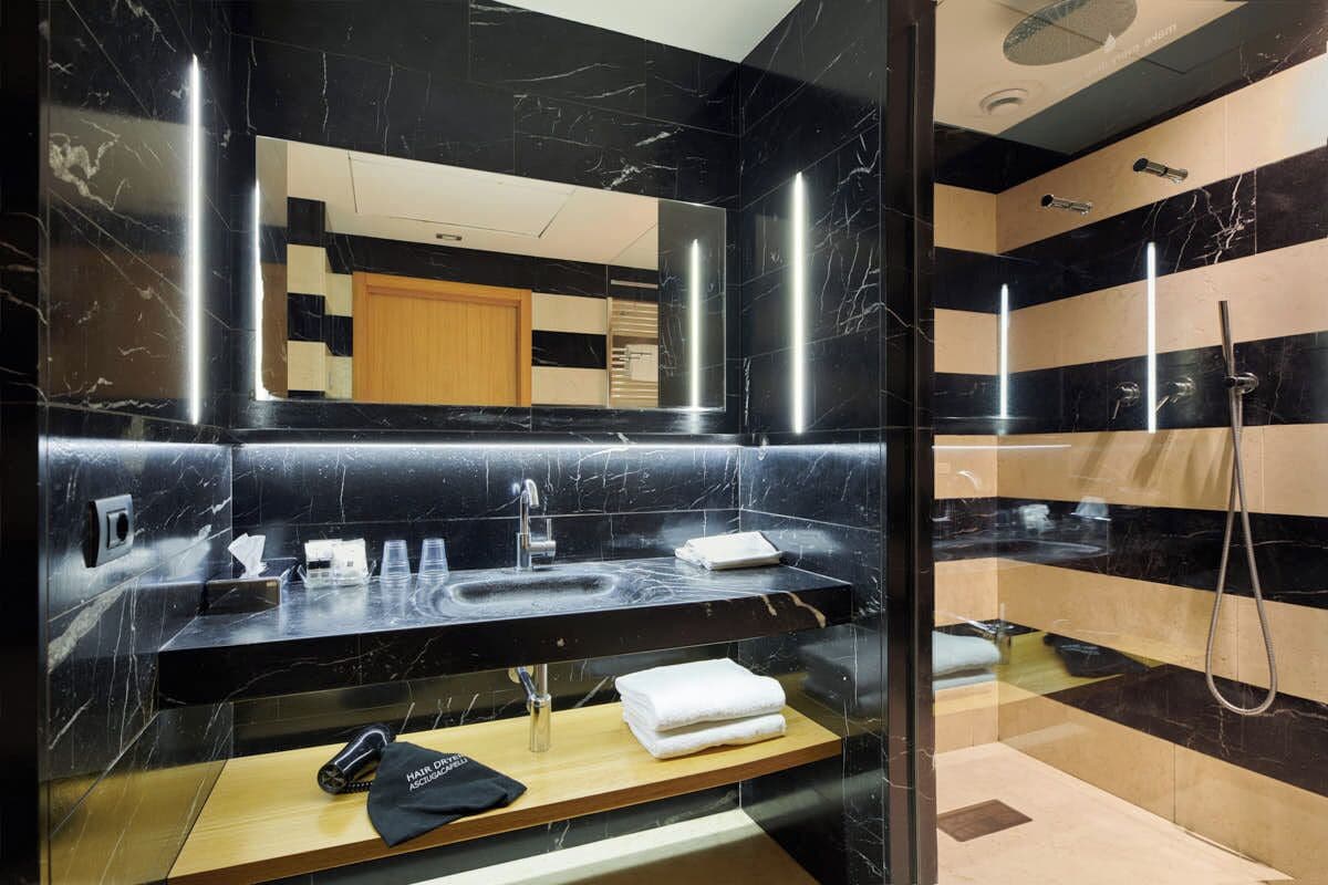 A modern bathroom with a black marble vanity, a large mirror, and a shower area.
