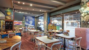 A restaurant interior with tables, chairs, a vintage refrigerator, and a large window with a view of the street.