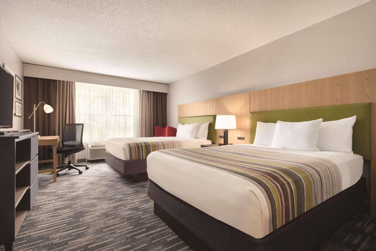 A hotel room with two beds, a desk, a chair, and a large window with curtains.