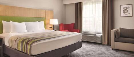 Habitación de hotel con una cama grande, una silla roja, un sofá gris, una ventana con cortinas y una obra de arte colgada en la pared.