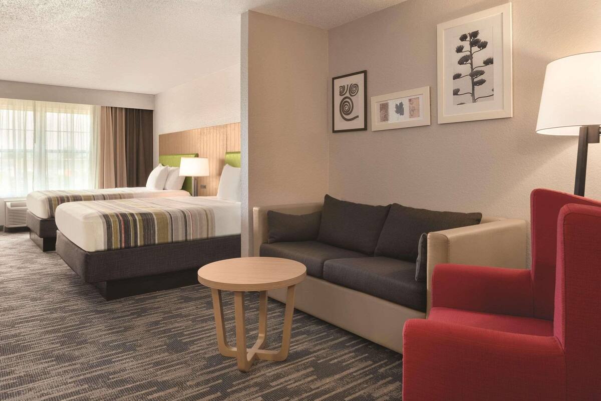 A hotel room with a bed, a sofa, a red armchair, a small round table, and framed artwork on the wall.