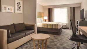 A hotel room with a sofa, a bed with a striped blanket, a desk with a chair, and a television.