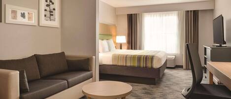 Habitación de hotel con sofá, cama con manta a rayas, escritorio con silla y televisión.