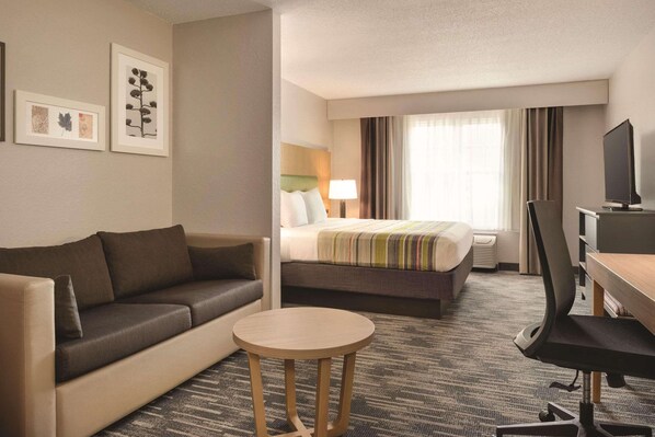 A hotel room with a sofa, a bed with a striped blanket, a desk with a chair, and a television.
