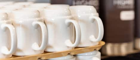 A stack of white ceramic mugs with handles, arranged on a shelf.