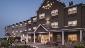 A Country Inn & Suites building with a dark exterior, multiple windows, and a well-lit entrance area.