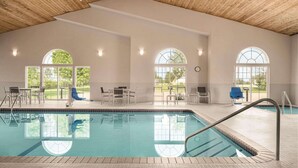 An indoor swimming pool with clear glass walls, wooden ceiling, and a view of the outdoors.