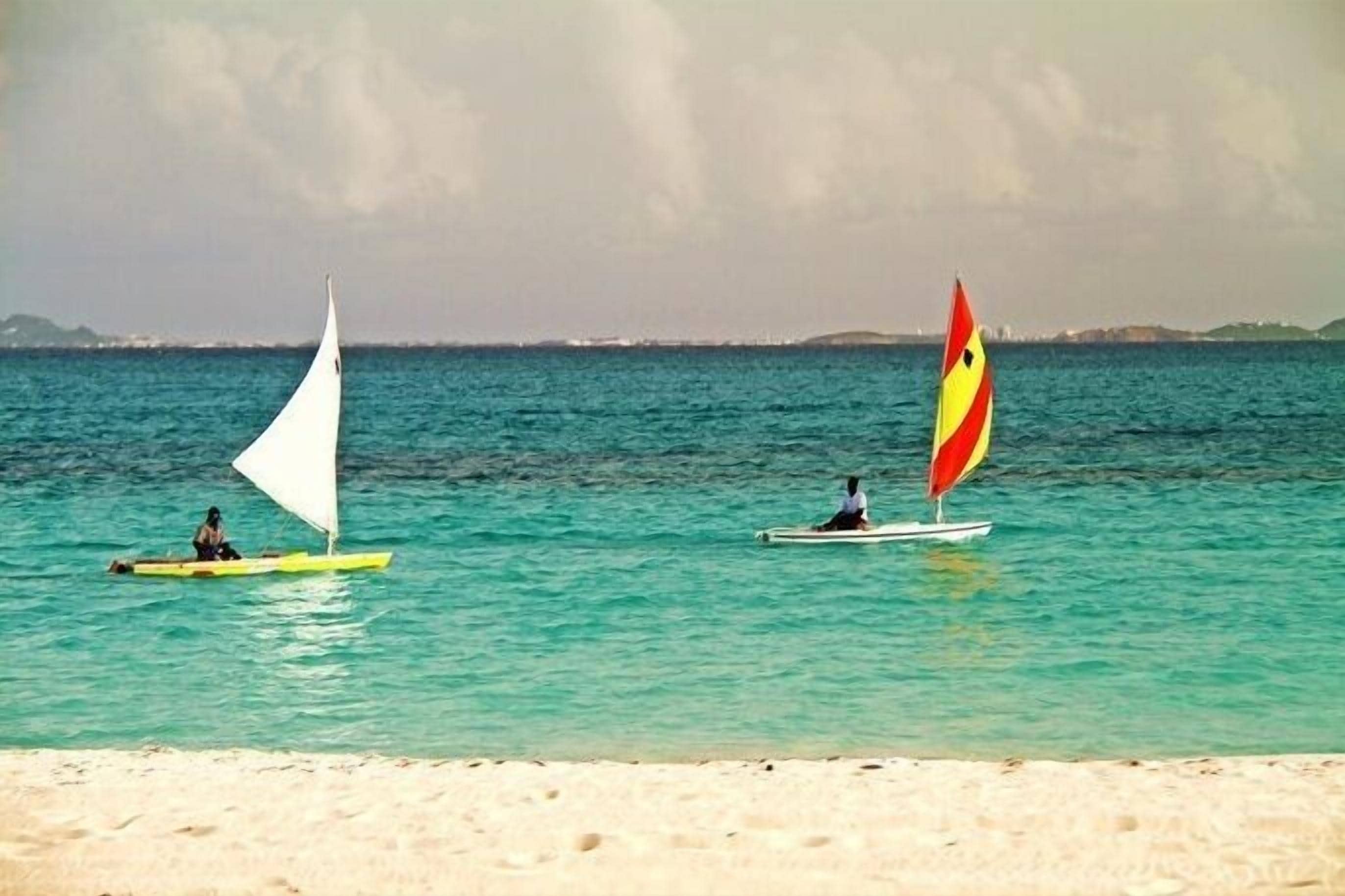 Dos veleros en un mar tranquilo con una playa arenosa al frente.