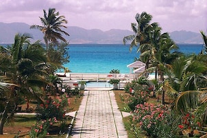 A pathway leading to a pool with a view of the ocean and mountains in the background.