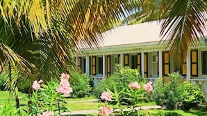 A colonial-style building with a covered porch, surrounded by lush greenery and flowering plants.