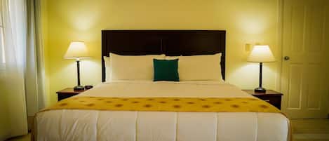 A hotel room with a large bed, two bedside lamps, and a door.
