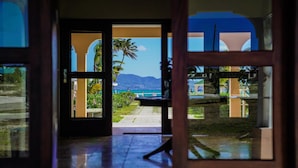 A doorway leading to a balcony with a view of a beach and mountains.