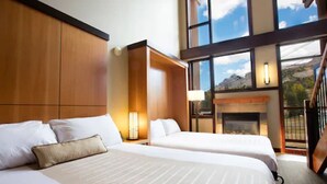 A hotel room with two beds, a fireplace, and large windows offering a mountain view. - Sunshine Mountain Lodge (Sunshine)