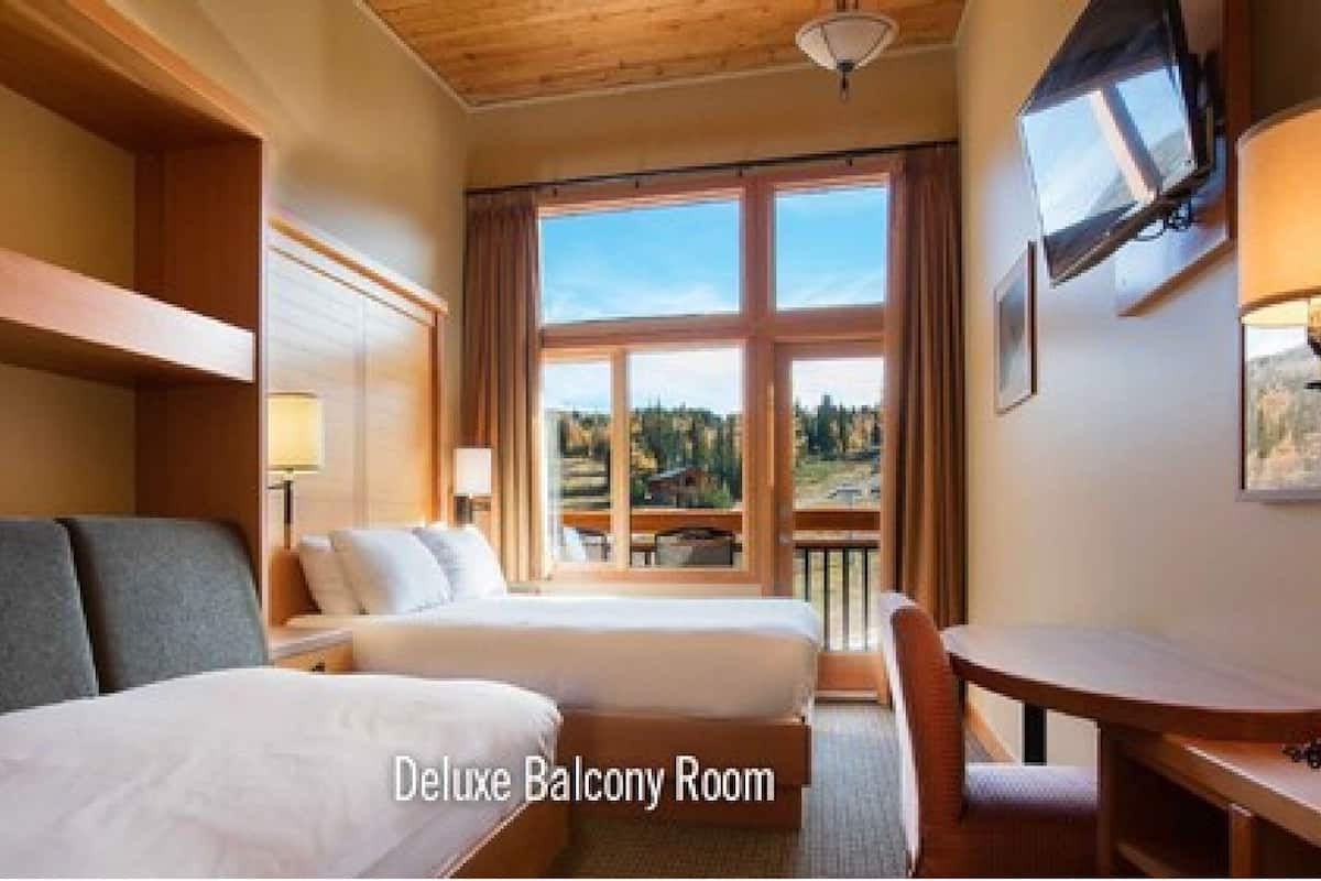 Habitación Deluxe con balcón, dos camas, escritorio, silla, televisor y vistas al exterior.